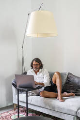 Man using laptop while sitting on sofa at home - DLTSF01162