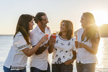 Parents with daughters toasting drinks while standing against sea during sunset - DLTSF01188