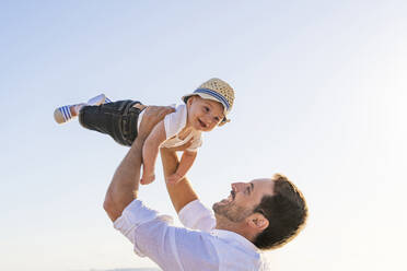 Lächelnder Vater, der seinen süßen Sohn gegen den klaren Himmel bei Sonnenuntergang abholt - DLTSF01194