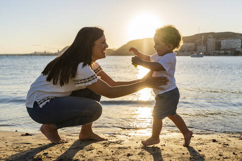 Cheerful mother playing with son at beach during sunset stock photo