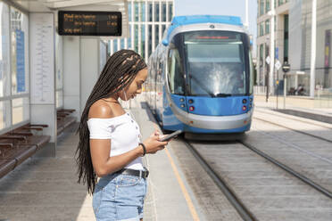 Young woman using phone while standing at tramway - WPEF03366