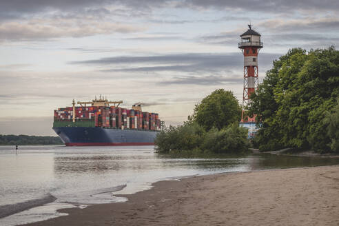 Germany, Hamburg, Container ship on Elbe river and Wittenbergen lighthouse at sunset - KEBF01672