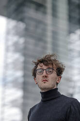 Close-up of serious young man wearing eyeglasses against building - OGF00565