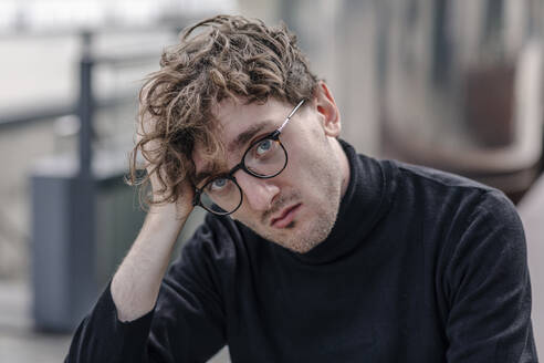 Close-up portrait of sad young man with head in hands sitting outdoors - OGF00569