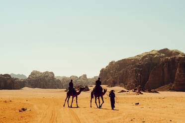 Touristen reiten auf Kamelen mit einem Beduinenführer in Wadi Rum, Jordanien - CAVF88965