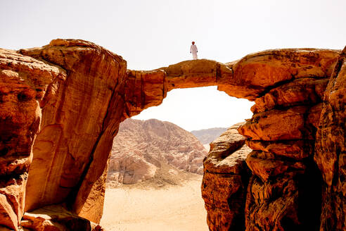 A Bedouin man stands atop a rock arch in Wadi Rum, Jordan - CAVF88986