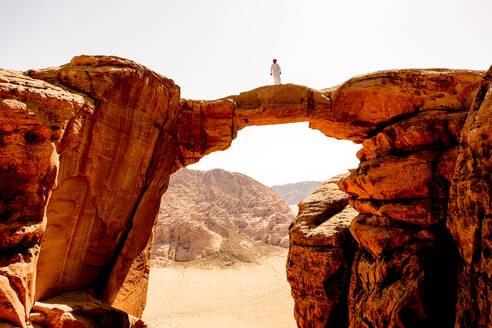 Ein Beduine steht auf einem Felsbogen in Wadi Rum, Jordanien - CAVF88986