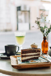 Scheibe Schokoladenkuchen, Blumen, Tasse Tee auf dem Tisch in einem Café im Freien - CAVF89074