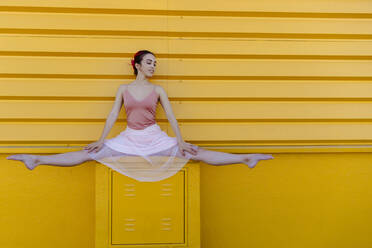 Ballerina im Spagat auf dem Sitz vor der gelben Wand - TCEF01068