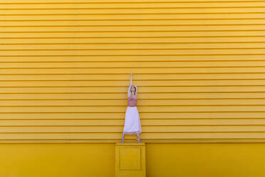 Ballerina auf Zehenspitzen tanzt auf Sitz gegen gelbe Wand - TCEF01072
