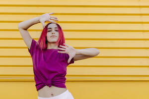 Selbstbewusste junge Frau mit gefärbtem Haar tanzt gegen eine gelbe Wand - TCEF01078
