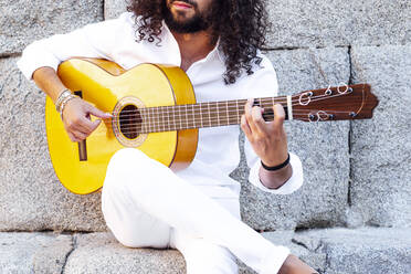 Guitarist playing flamenco while sitting against concrete wall - JCMF01396