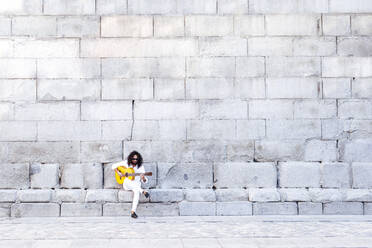 Flamenco-Gitarrist spielt Gitarre und sitzt auf einer Bank an einer Betonwand - JCMF01398