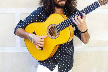 Mann spielt Gitarre, während er an der Wand steht - JCMF01403