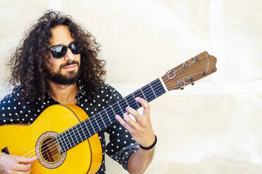 Mann mit Sonnenbrille spielt Gitarre und steht an der Wand - JCMF01404