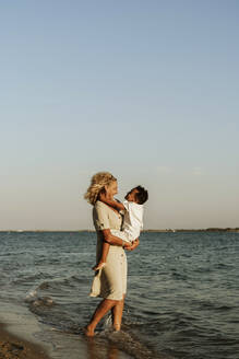 Grandmother picking up grandson at beach during sunset - ERRF04345