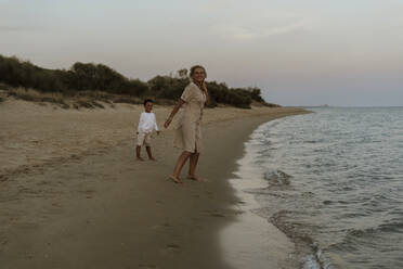 Großmutter und Enkel stehen am Strand bei Sonnenuntergang - ERRF04363