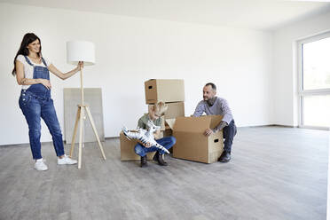 Pregnant mother holding electric lamp while father and son crouching on floor with toy and cardboard box - MJFKF00647