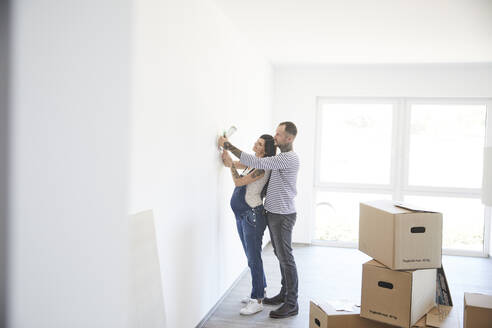 Heterosexual couple trying light fixture on wall at new home - MJFKF00650