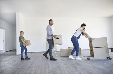 Family keeping cardboard boxes on skateboard in new house - MJFKF00651