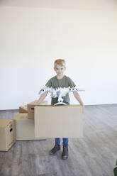 Cute little boy holding cardboard box with toy on it in new house - MJFKF00655