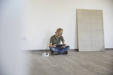 Little boy playing on digital tablet in new house - MJFKF00657