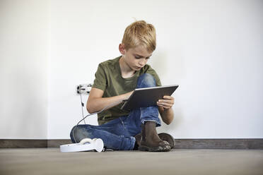 Little boy playing on digital tablet while sitting in new house - MJFKF00662