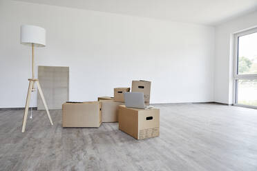 Interior of modern room with cardboard boxes, electric lamp and laptop - MJFKF00666
