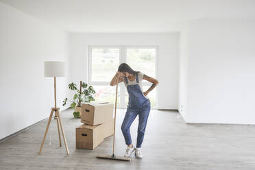 Pregnant woman with hand on hip holding mop while standing at new home - MJFKF00681