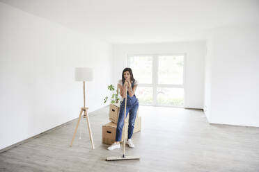 Pregnant woman standing with mop at new home - MJFKF00682