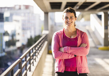 Smiling young woman with arms crossed standing on terrace - UUF21373