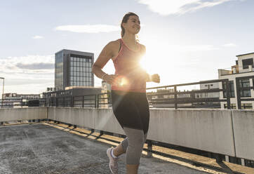 Weibliche Athletin läuft auf Terrasse gegen Himmel in Stadt - UUF21376