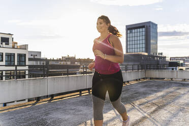Lächelnde Sportlerin, die auf einer Terrasse gegen den Himmel in der Stadt läuft - UUF21377