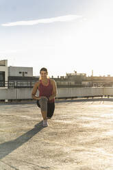 Lächelnde junge Frau beim Sport auf der Terrasse eines Gebäudes gegen den Himmel an einem sonnigen Tag - UUF21381