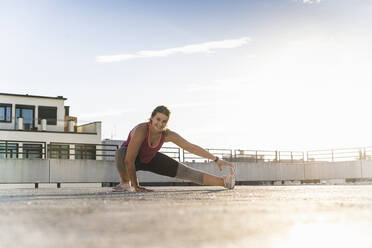 Smiling female athlete exercising on building terrace against sky - UUF21383