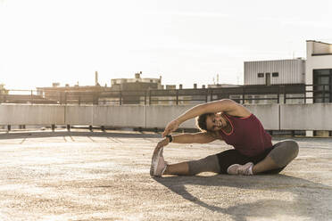 Smiling young woman with arms raised exercising on terrace against clear sky in city - UUF21384