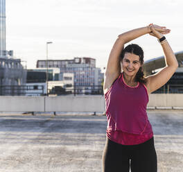 Junge Frau mit erhobenen Armen beim Sport auf der Terrasse gegen den Himmel - UUF21386