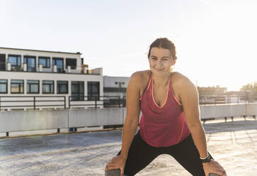 Smiling young woman exercising on terrace against clear sky during sunset - UUF21389