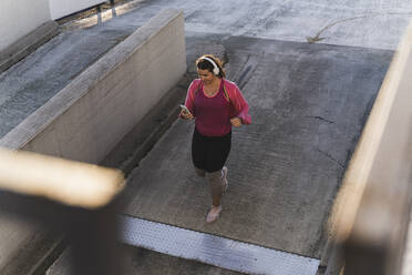 Young woman using mobile phone while running on terrace at sunset - UUF21401