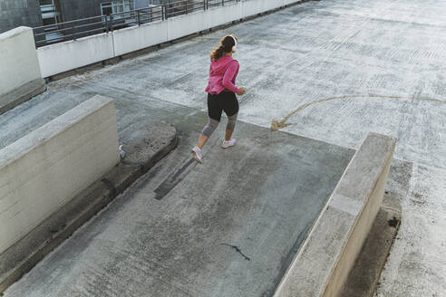 Weibliche Athletin hört Musik über Kopfhörer beim Joggen auf der Terrasse bei Sonnenuntergang - UUF21405