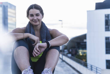 Lächelnde junge Frau mit Handtuch sitzt auf Terrasse gegen klaren Himmel bei Sonnenuntergang - UUF21422