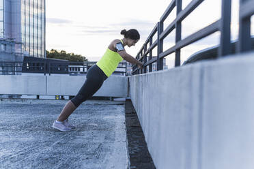 Young woman with arm band exercising on railing at sunset - UUF21424