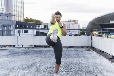 Young woman boxing and kicking on terrace at sunset - UUF21428