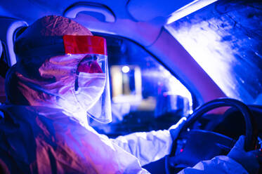 Mid adult man wearing protective suit driving ambulance at night - JCMF01419