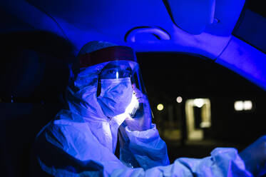 Male worker wearing workwear talking over mobile phone while driving ambulance at night - JCMF01423