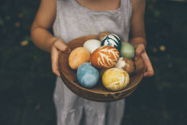 Baby girl holding bowl of colorful organically colored Easter eggs - MBEF01464