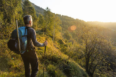 Älterer Mann mit Rucksack steht auf einem Berg im Wald während des Sonnenaufgangs, Orobie, Lecco, Italien - MCVF00581