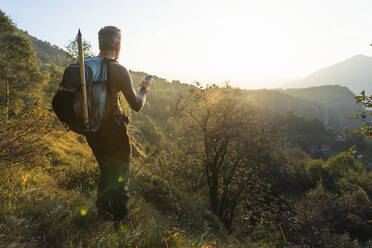 Älterer Mann benutzt sein Smartphone, während er bei Sonnenaufgang auf einem Berg steht, Orobie, Lecco, Italien - MCVF00582