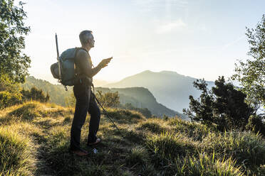 Man using mobile phone while standing on mountain against sky at sunrise, Orobie, Lecco, Italy - MCVF00585