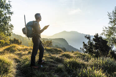 Mann, der ein Mobiltelefon benutzt, während er auf einem Berg gegen den Himmel bei Sonnenaufgang steht, Orobie, Lecco, Italien - MCVF00585